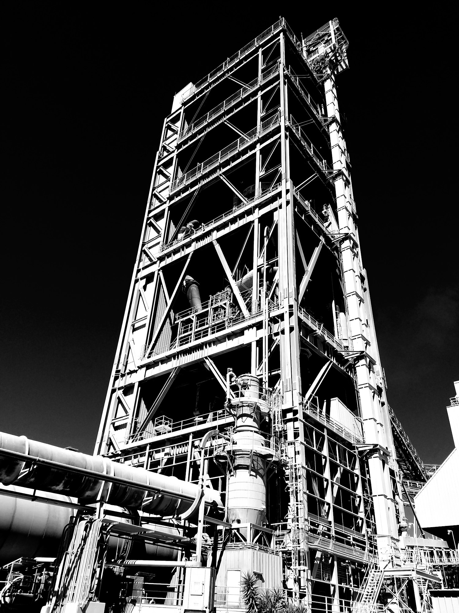 Black and white photo of a large industrial structure with pipes and scaffolding.