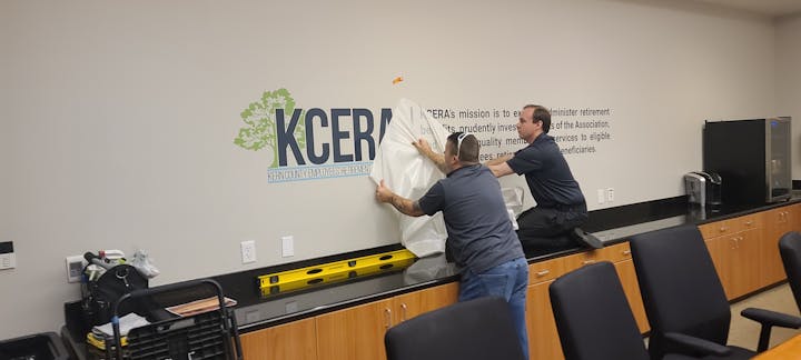 Two men applying vinyl lettering to a wall with organizational branding.