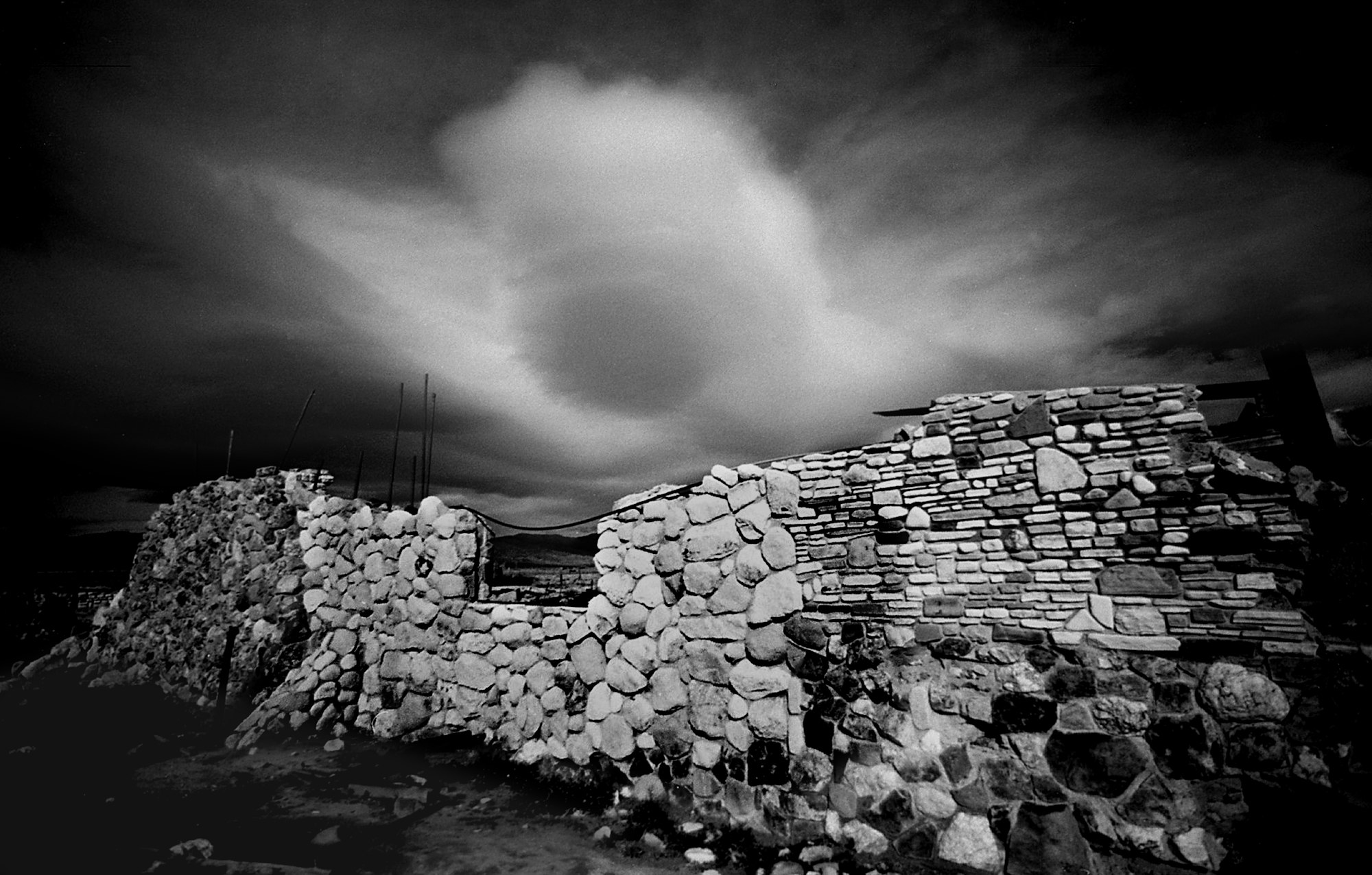 A black and white photo of a stone wall under dramatic skies.