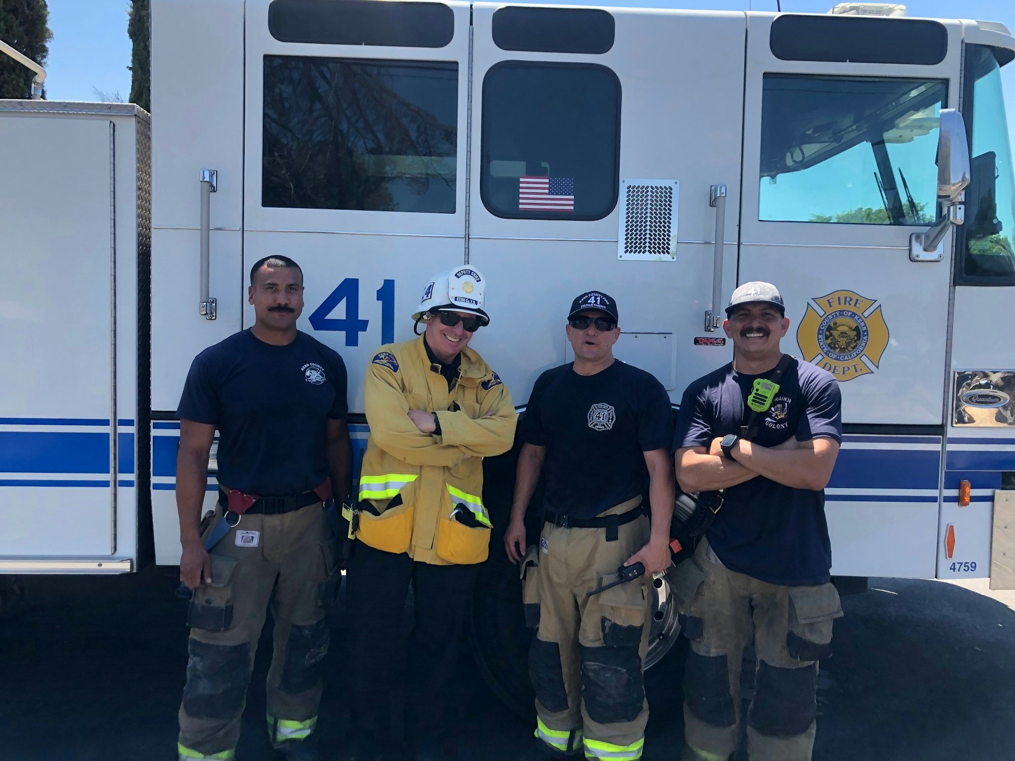 Four firefighters posing in front of a fire truck.