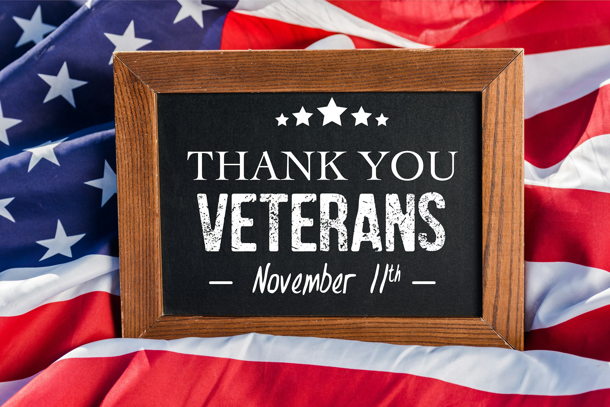 An American Flag with a small chalkboard on top of it with the words Thank You Veterans November 11th written in chalk on it.