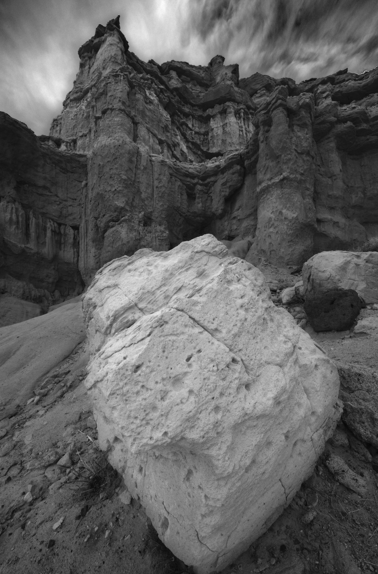A black and white photo of a large rock formation under a dramatic sky.
