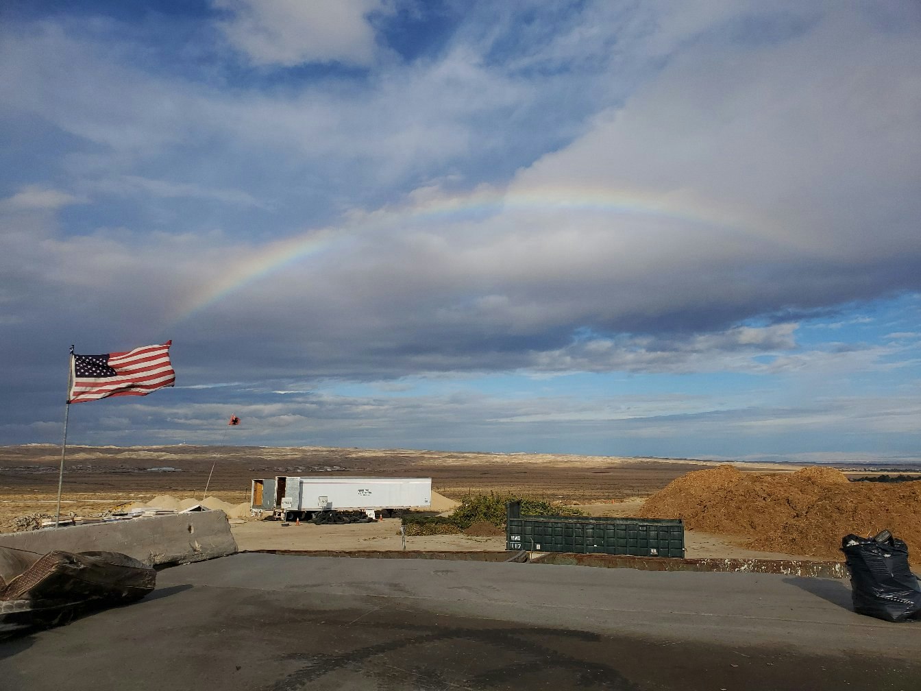 A rainbow, American flag, and construction materials on a cloudy day.