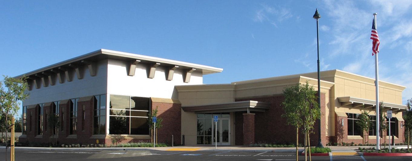 A modern building with a mix of brick and stucco, large windows, and landscaping, set against a blue sky.