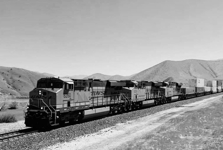 Black and white photo of a freight train with mountains in the background.