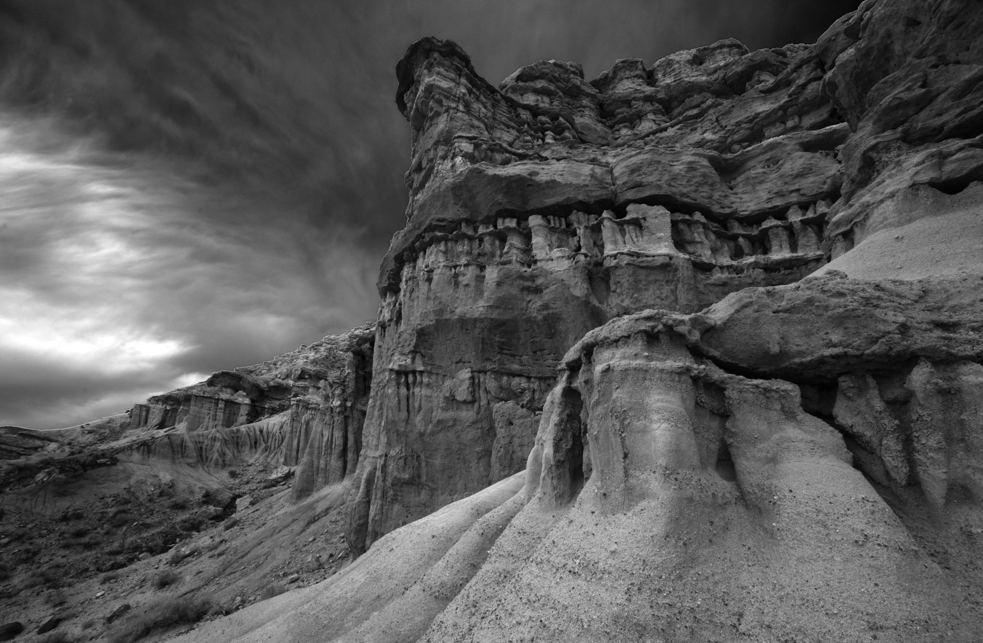 Dramatic black and white landscape with eroded rock formations under a textured sky.