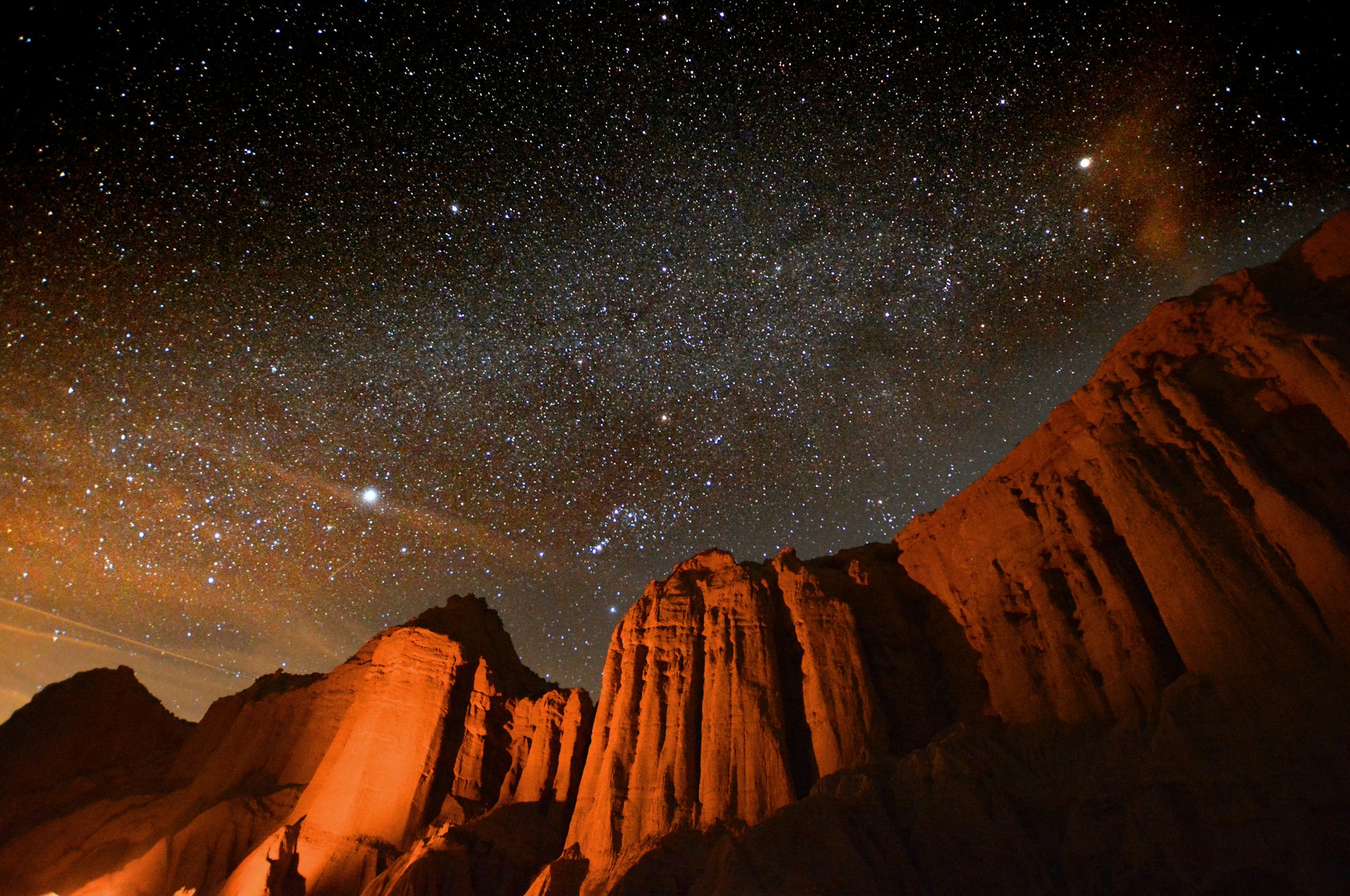 A starry night sky above orange-lit rock formations.
