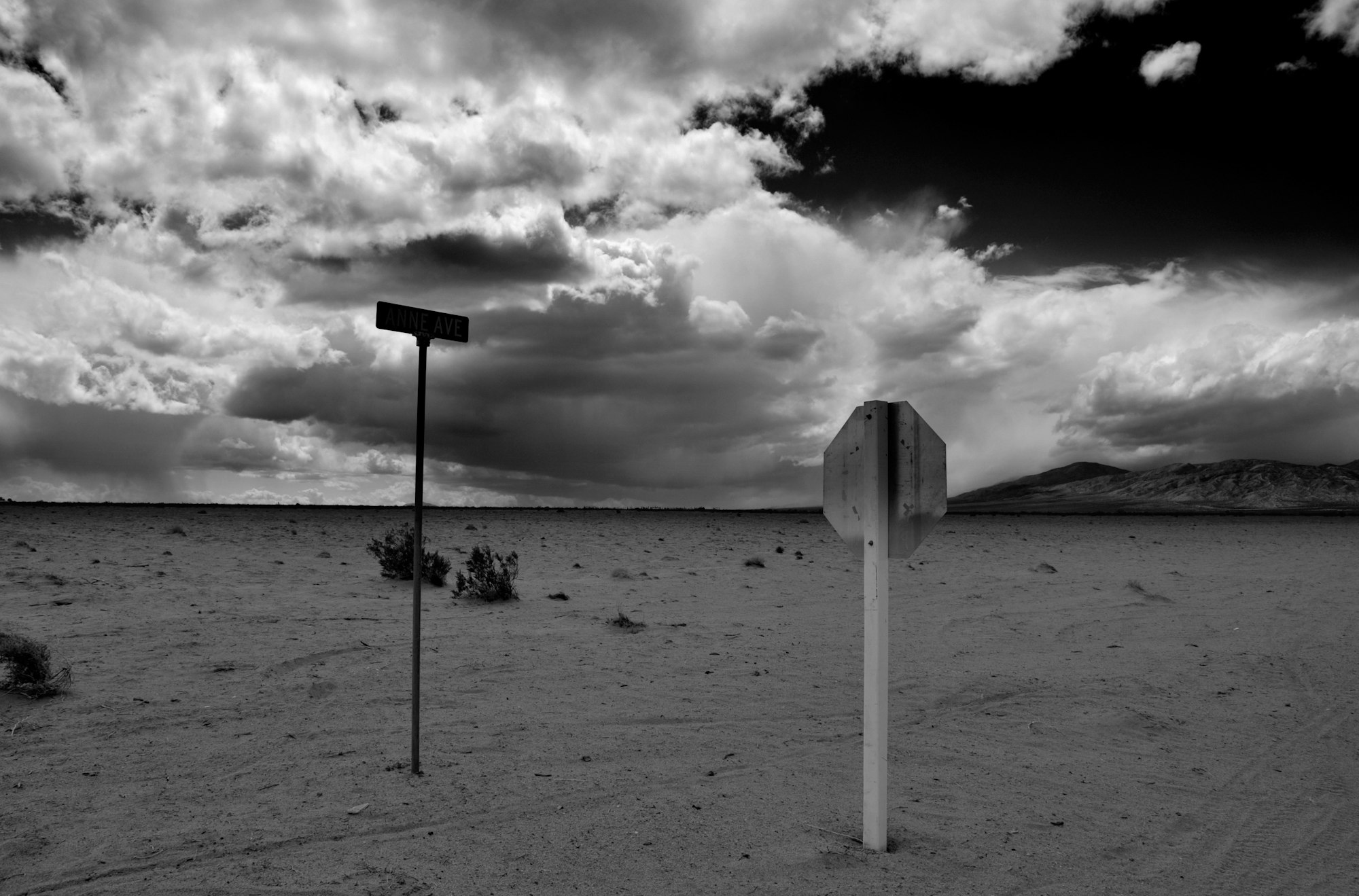 Street signs in a desolate landscape under a dramatic cloudy sky. Black and white.