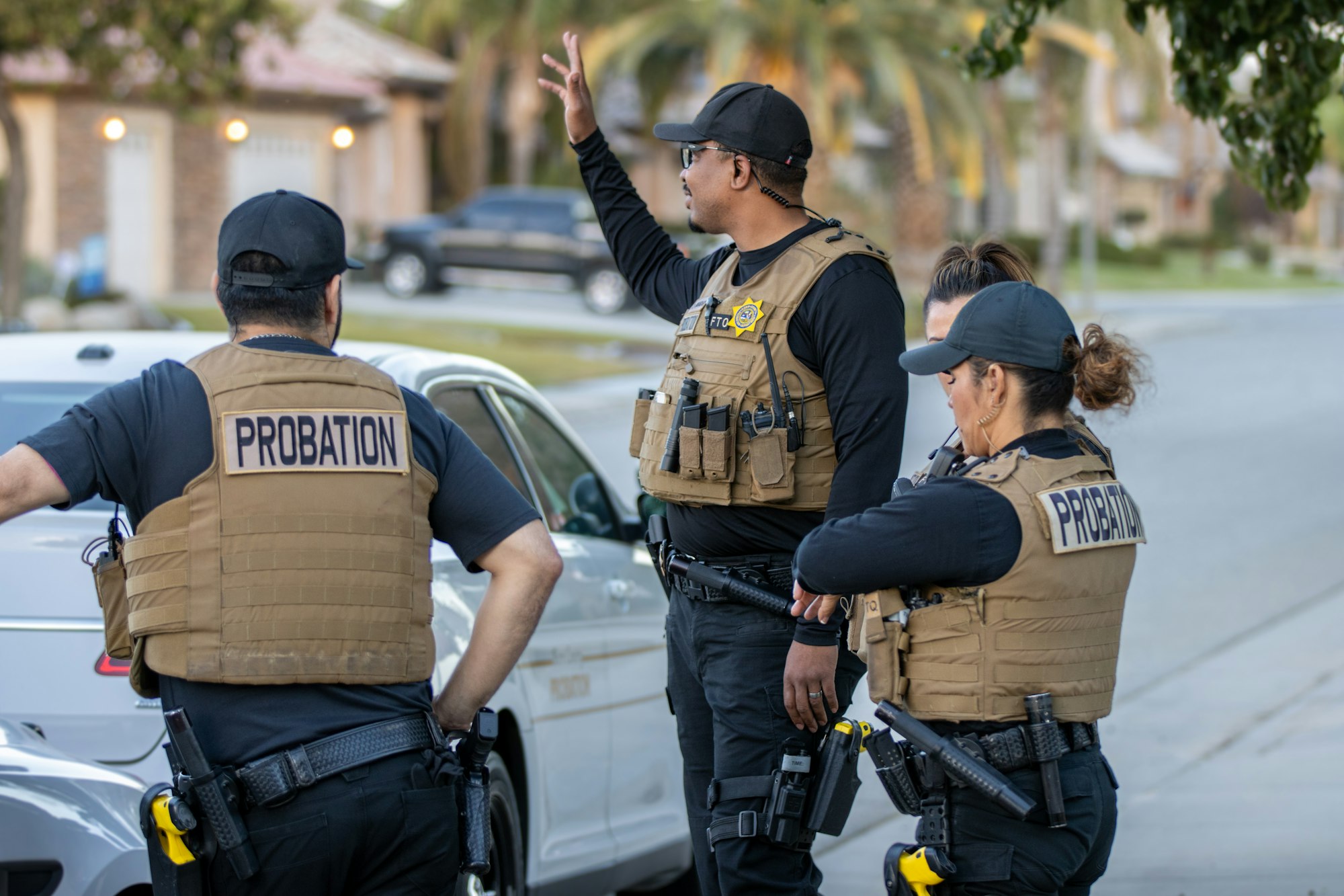 Three probation officers wearing tactical vests labeled "PROBATION," engaged in a conversation.