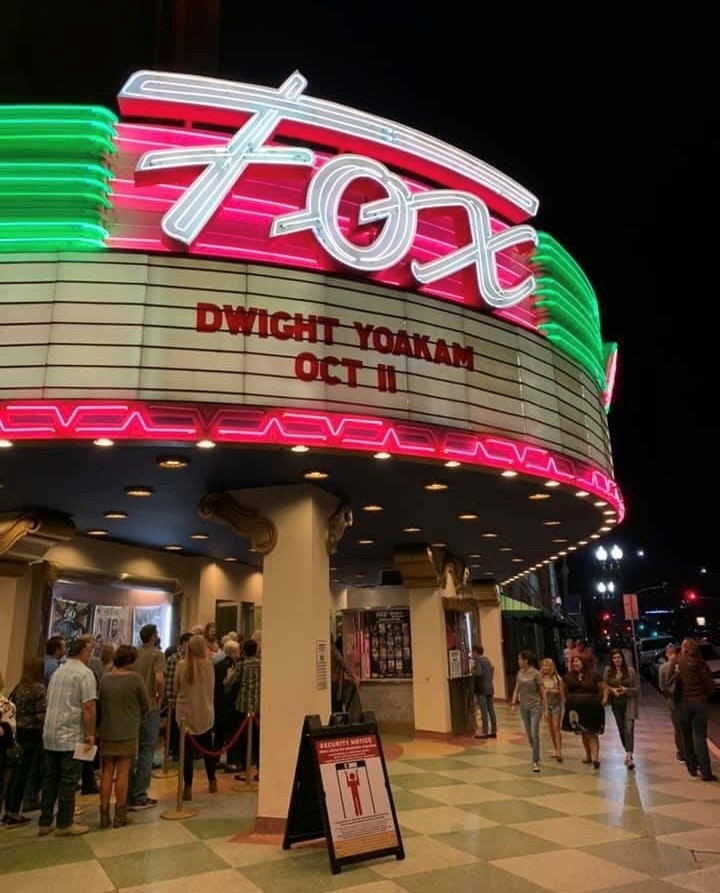 Vintage theater marquee with neon lights, people queuing, and an event sign for Dwight Yoakam.