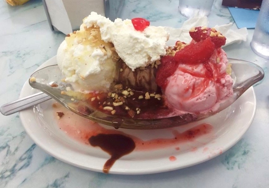 A banana split with various ice cream flavors, whipped cream, nuts, syrup, and a cherry on top.