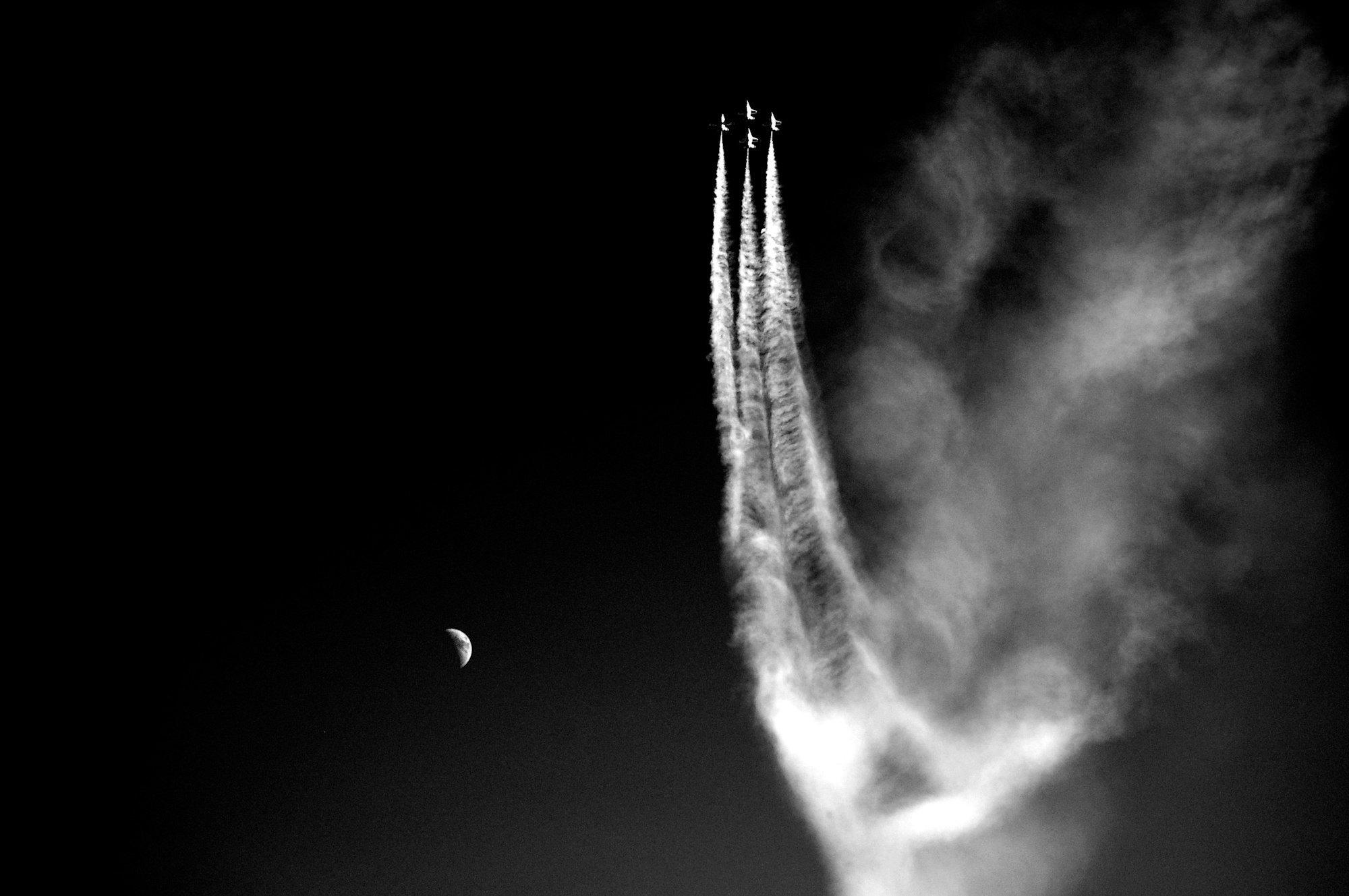Four jets flying in formation with contrails against a dark sky, crescent moon visible.