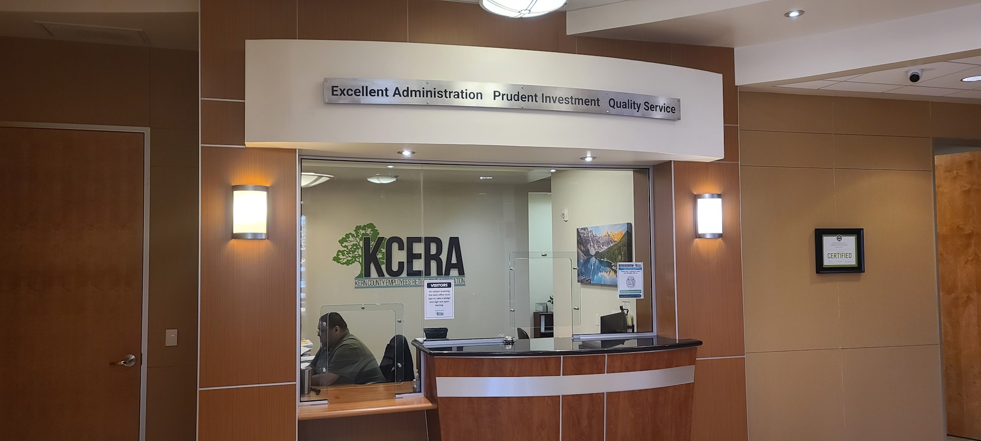 KCERA reception area with signage, a person at the desk, a landscape painting, "KCERA" logo, and wood-toned interiors.
