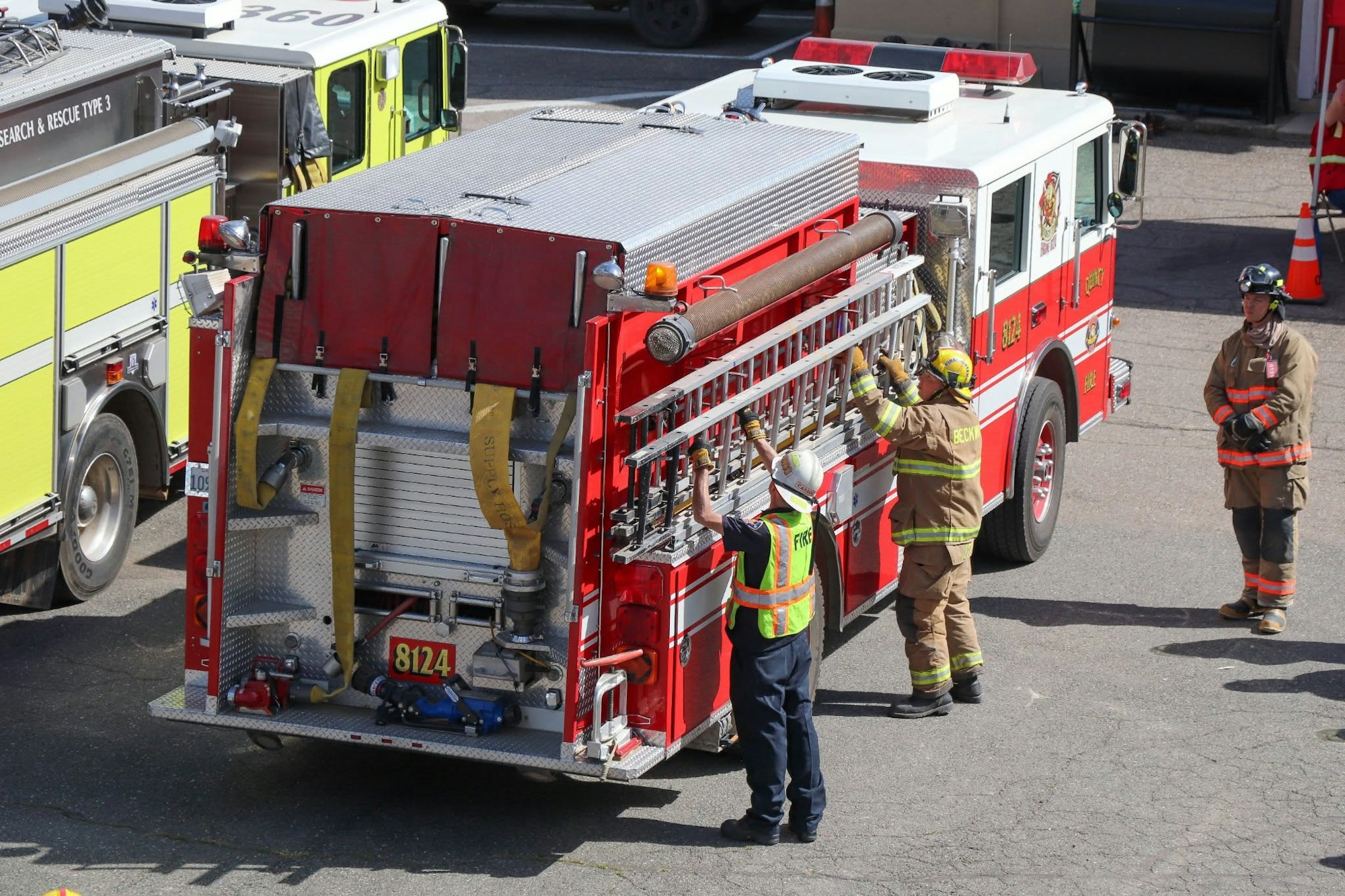 Firefighters handling equipment on a red fire truck 81 24, with another fire truck nearby.