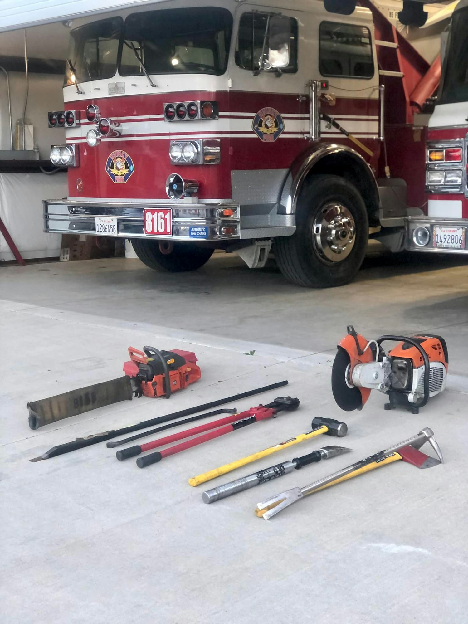 Fire truck 8161 and firefighting tools, including saws, axes, and pry bars, arranged on the ground.