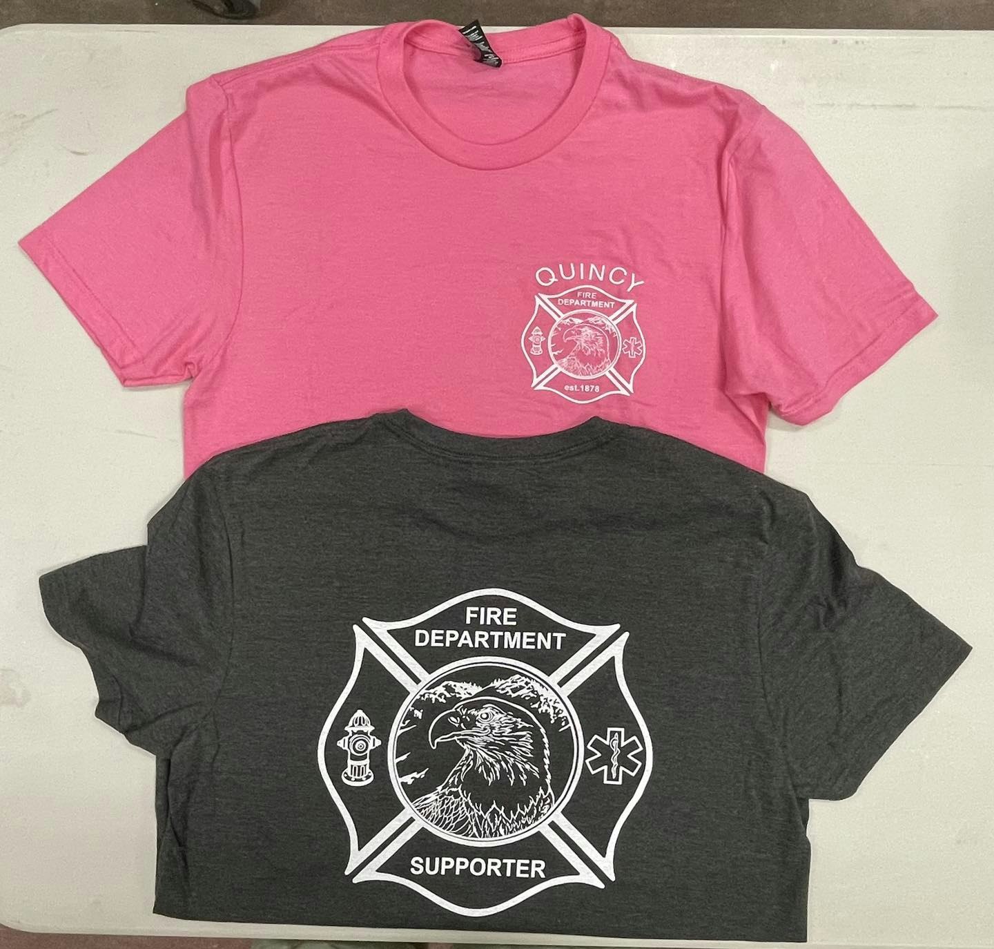 Two t-shirts with fire department logos, one pink and one gray.