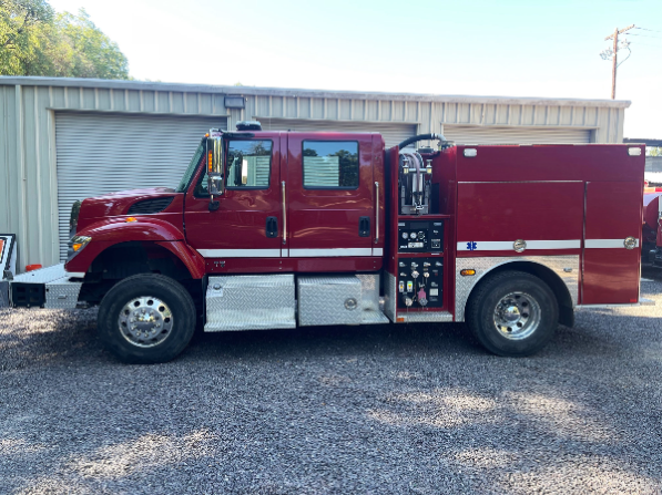 A red fire truck parked on a gravel surface in front of a metal building with a closed garage door.
