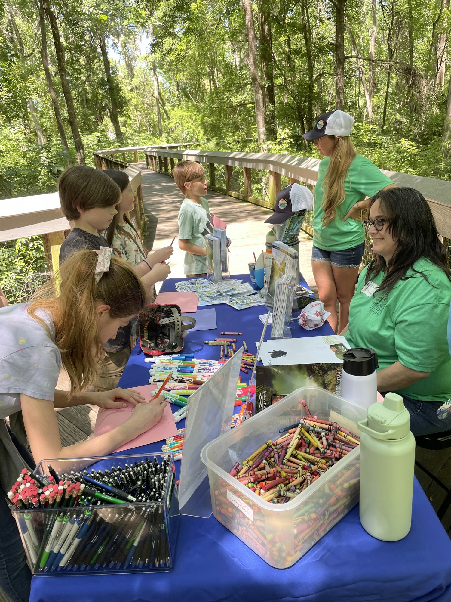 Outdoor coloring activity with children and adults at a table with crayons and markers.