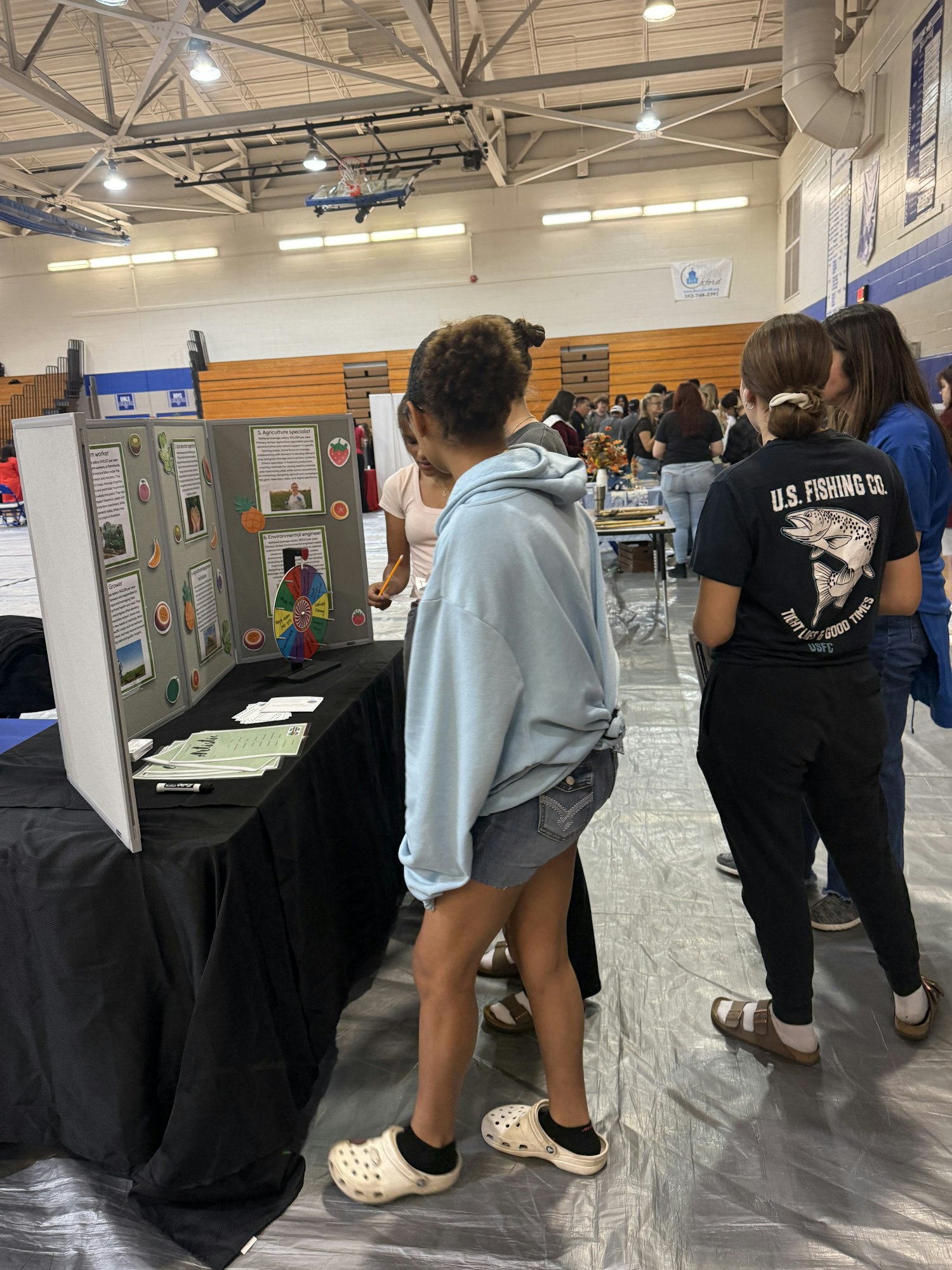 A science fair with students presenting projects; informational posters on display tables. (Please rotate your device for proper orientation.)