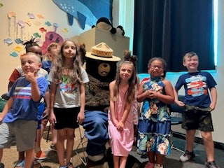 Group of kids posing with a character in a bear costume indoors.