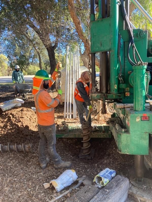Workers in safety gear operate a drilling machine on a construction site, surrounded by tools and materials.