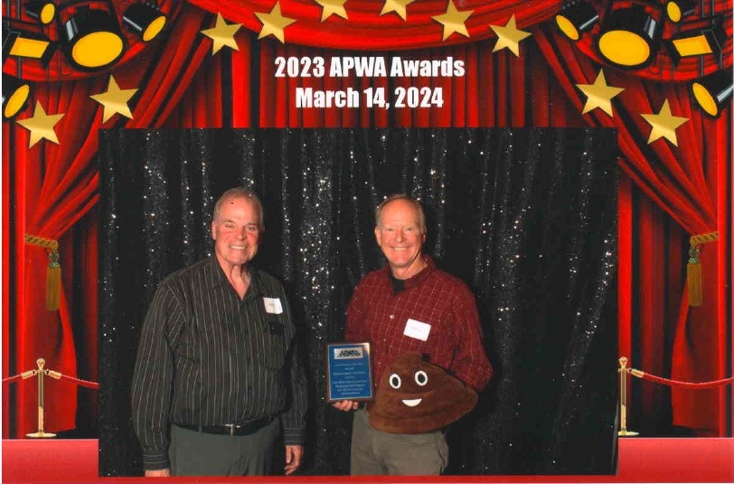 Two individuals at an awards event, holding a plaque, with a celebratory backdrop dated March 14, 2024.