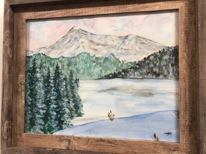 A framed watercolor painting of a mountainous landscape with evergreen trees and a snow-covered field.