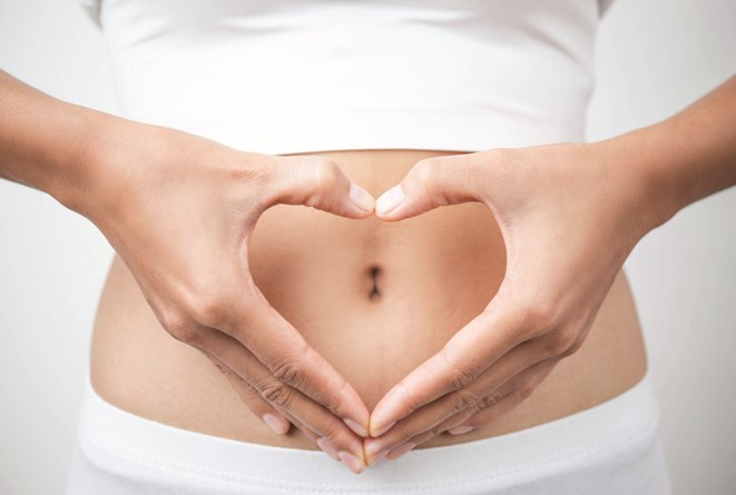 Hands forming a heart shape over a belly.