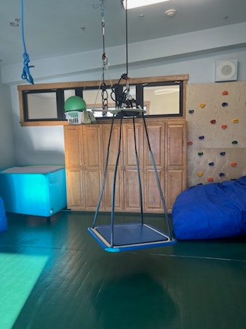 A room with a hanging swing, climbing wall, bean bags, and cupboard.