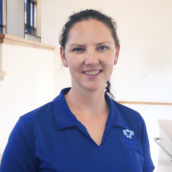 A smiling person in a blue shirt with a logo, indoors.