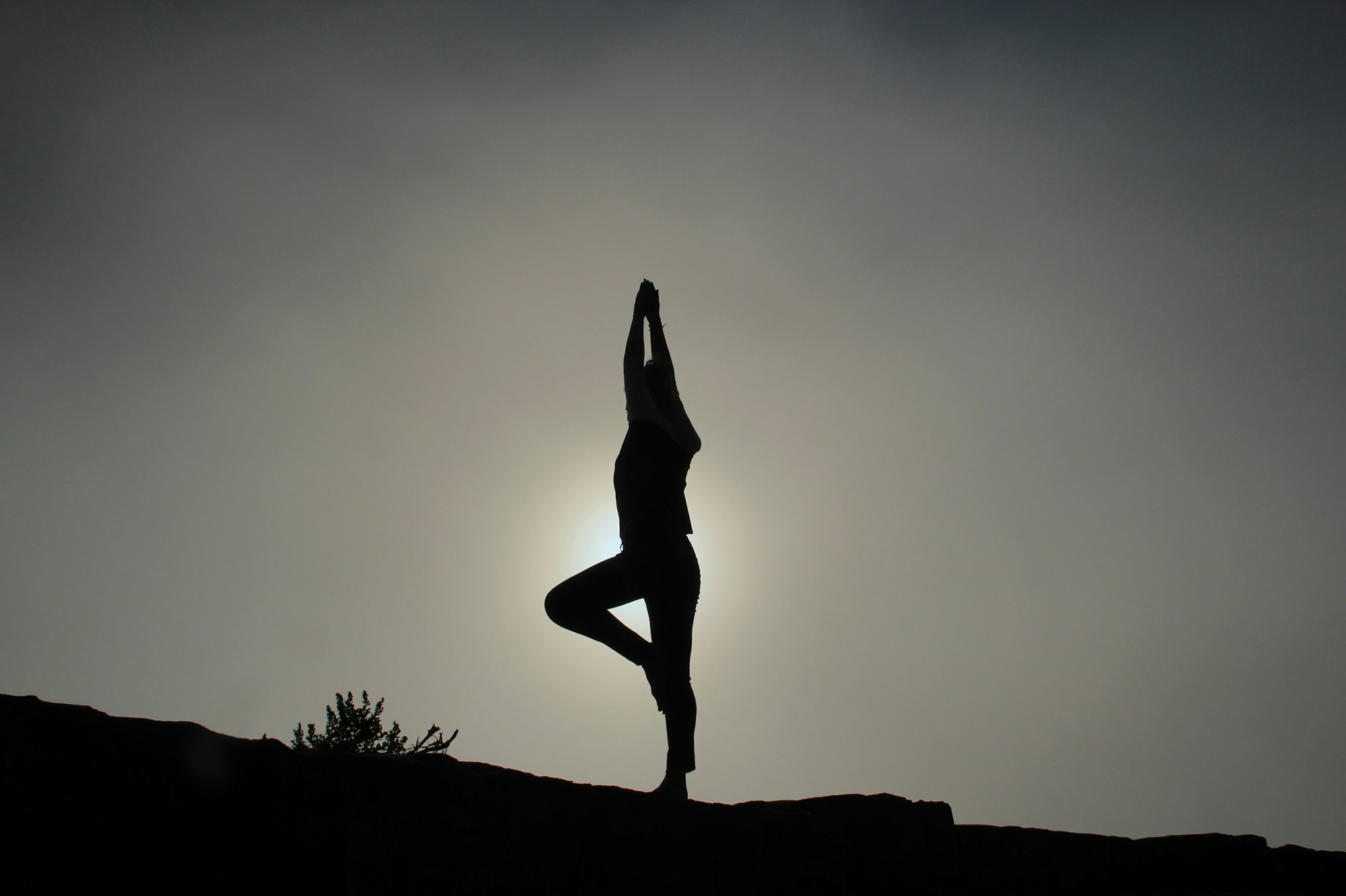Silhouette of a person doing a yoga pose against a bright sky.