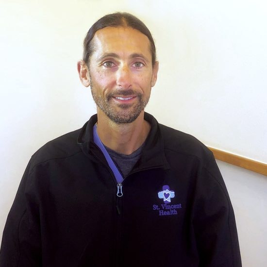 A smiling person wearing a jacket with a “St. Vincent Health” logo.