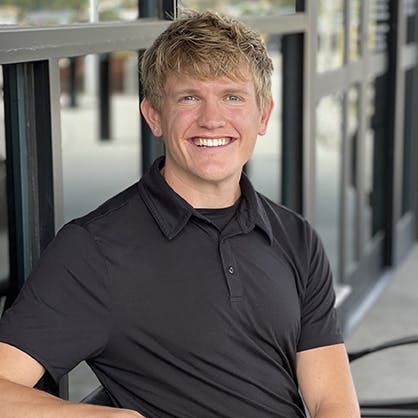 Jordan Winters smiles while sitting on an outdoor bench, wearing a black polo shirt.
