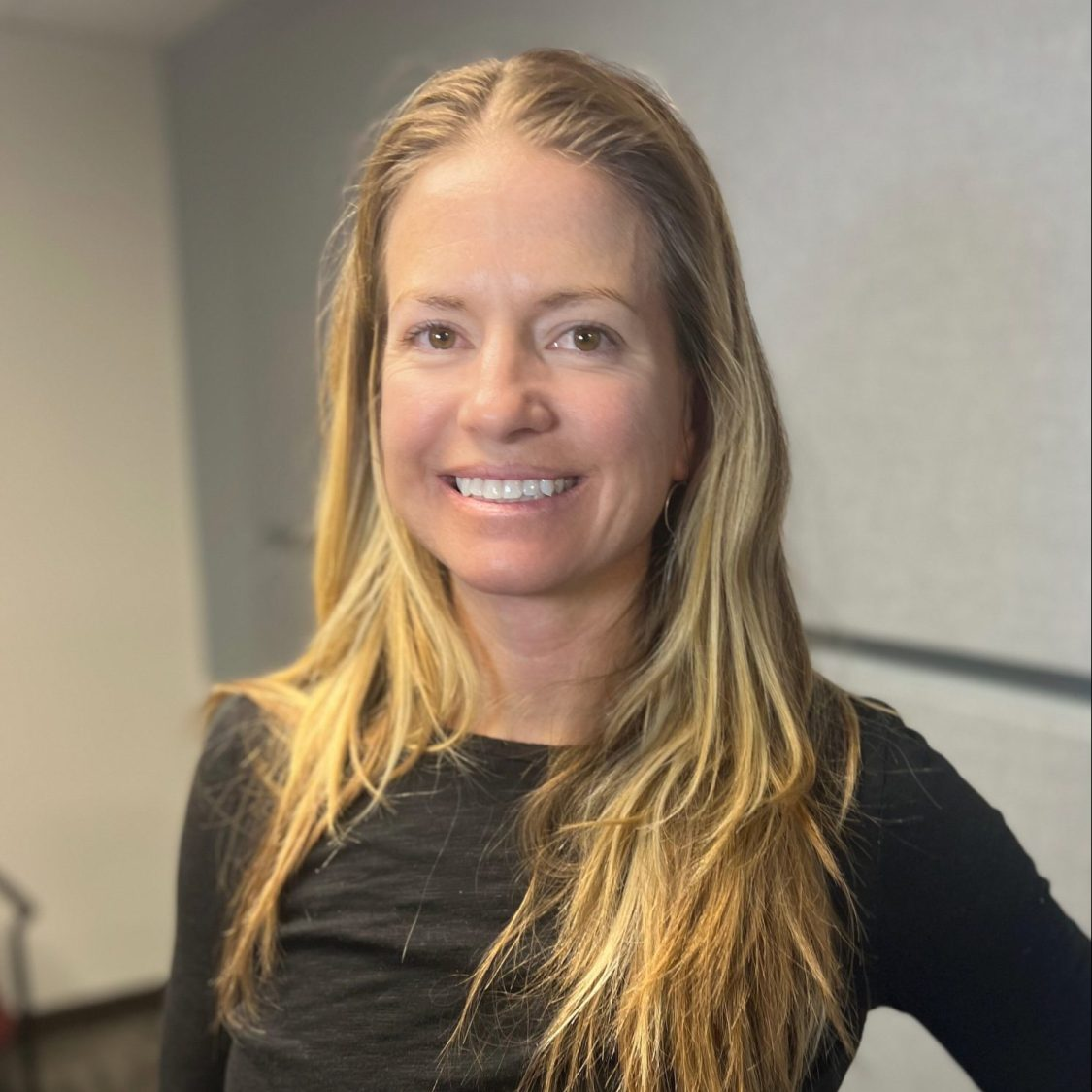 A smiling woman with long blonde hair wearing a black top.