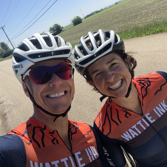 Dr. Noxon and a cyclist in helmets smiling, with matching jerseys and a field in the background.