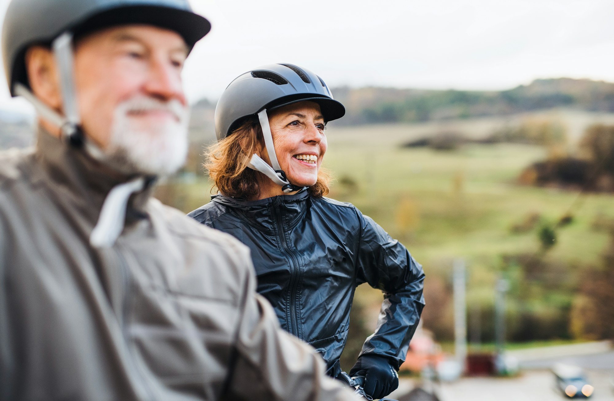 Smiling older male and female in bicycle helmets and rain jackets.