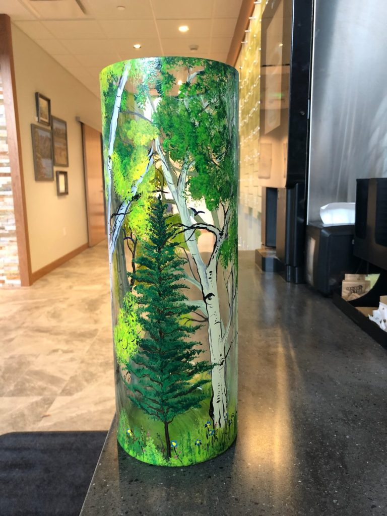 A decorated cylindrical object with a forest scene, indoors near a water dispenser.