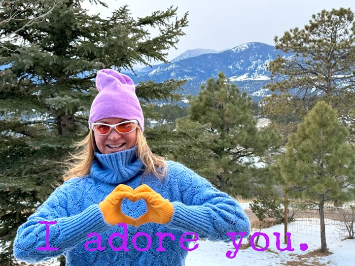 Dr. Sonja Stilp gesturing a heart with their hands, wearing winter attire, with snowy mountains and trees in the background, accompanied by the text "I adore you."