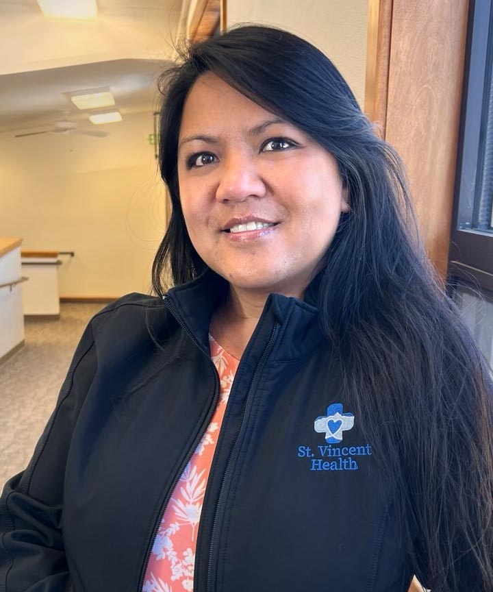 Michelle Sweet wearing a "St. Vincent Health" jacket standing indoors, smiling at the camera.