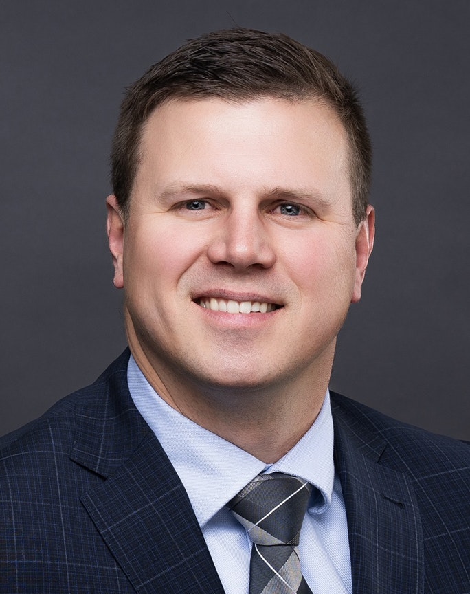 A person in a suit and tie smiling against a dark background.
