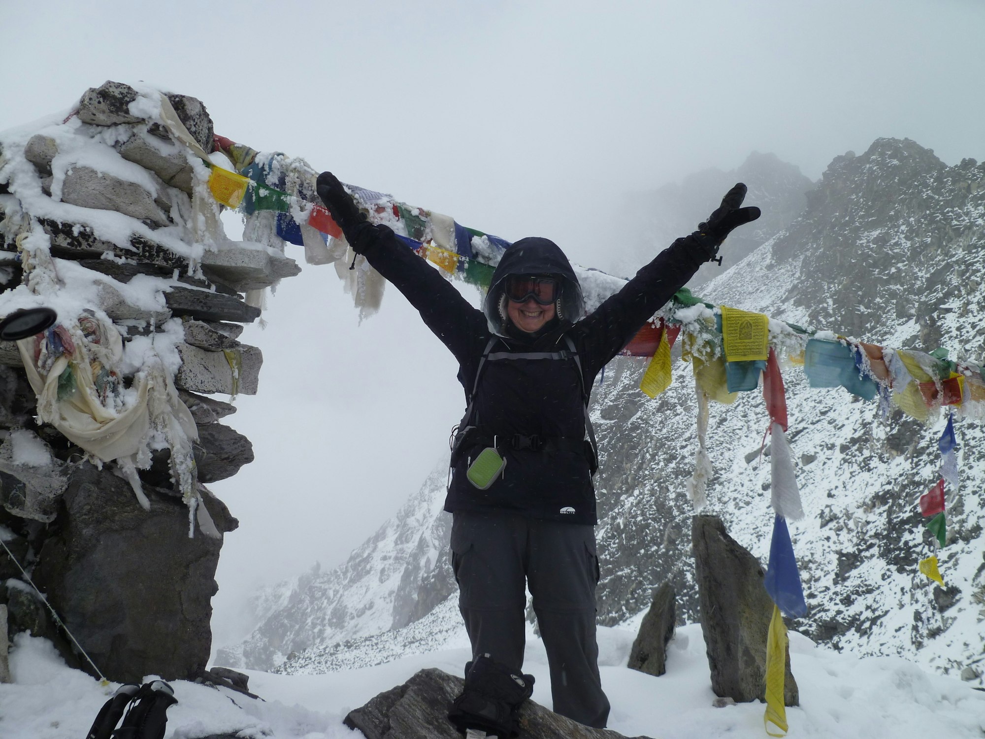 Person celebrating at a snowy mountain summit with colorful prayer flags.