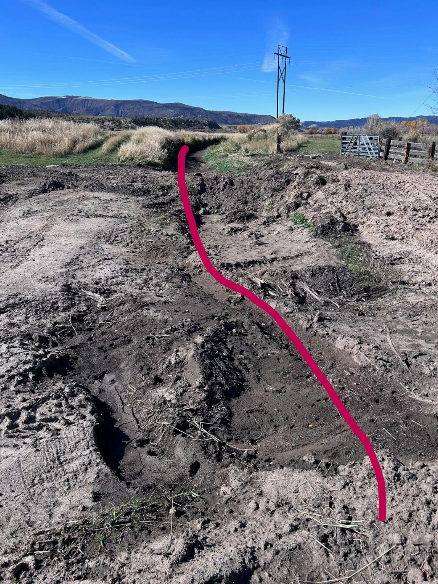 An irrigation ditch filled with post-fire debris run off, grass, power pole, and mountains under a clear blue sky.