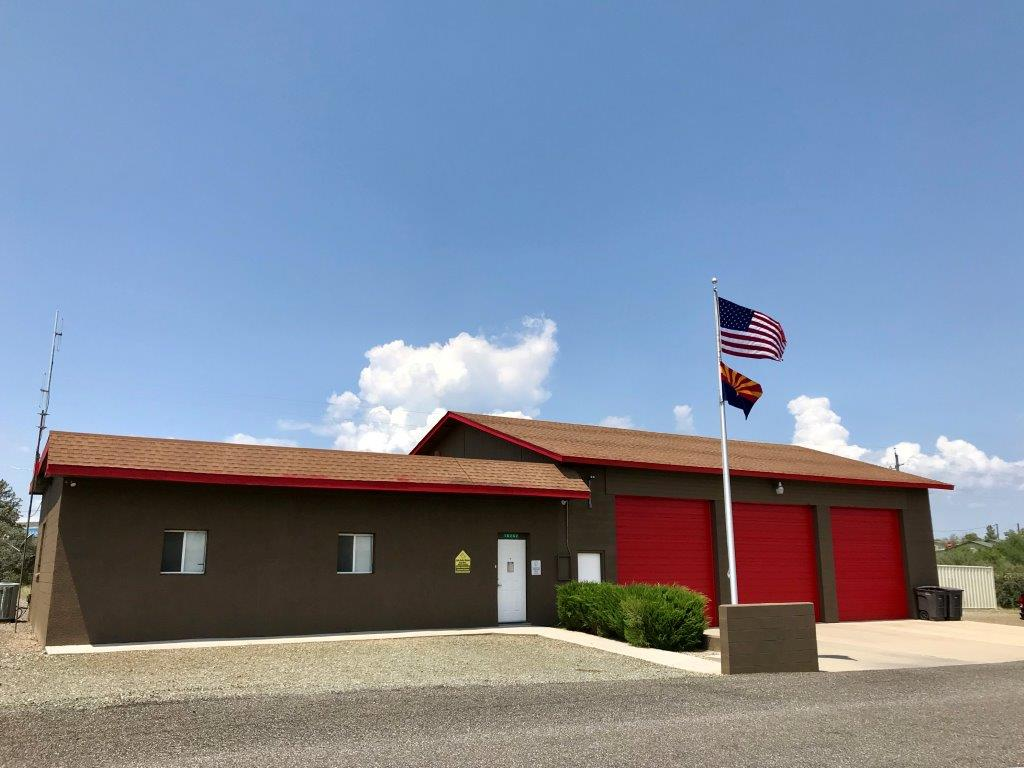 A brown building with red garage doors, two flags (USA and another), under a blue sky with clouds.