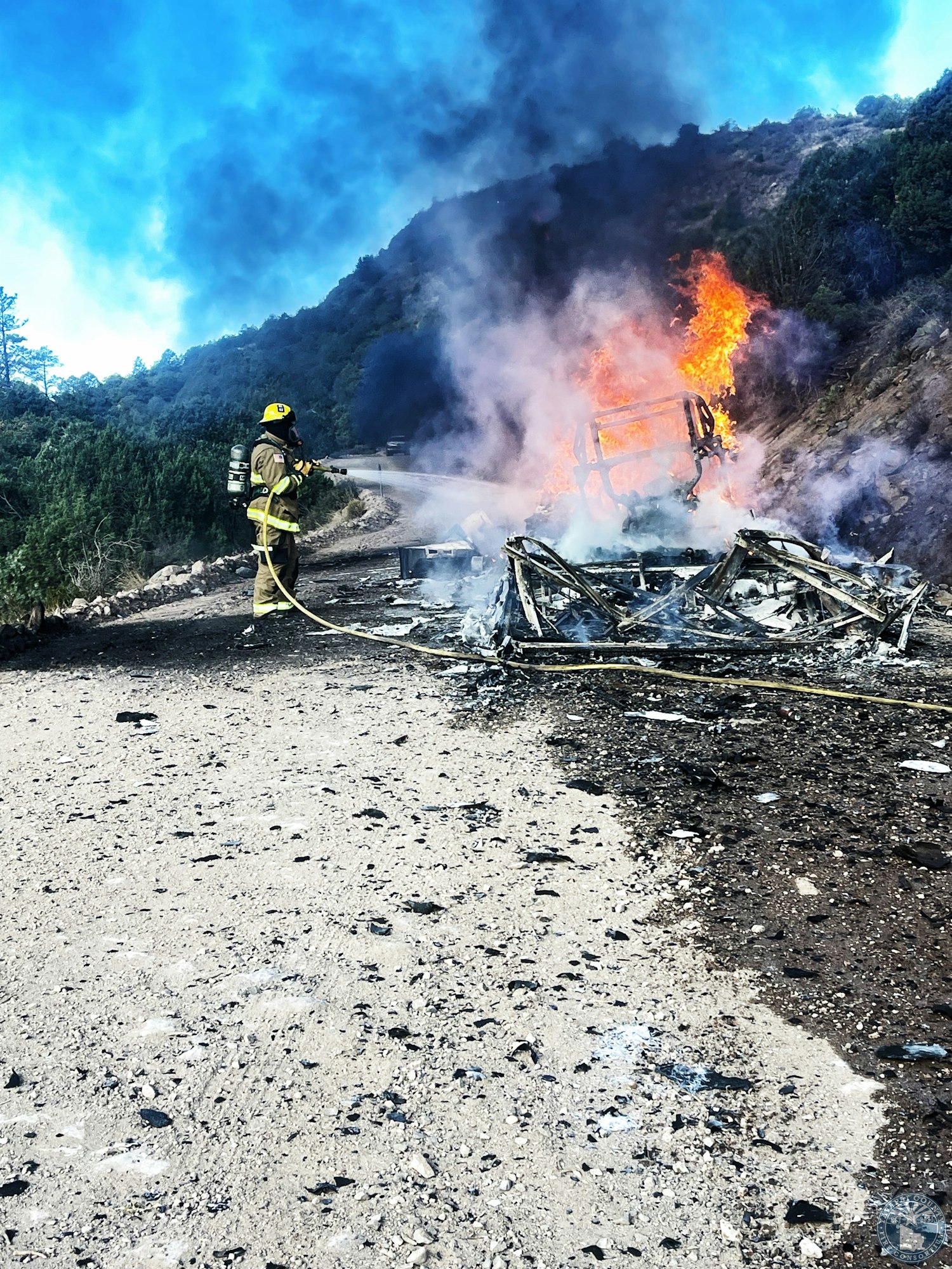 Firefighter extinguishing a burning vehicle on a mountainous road.