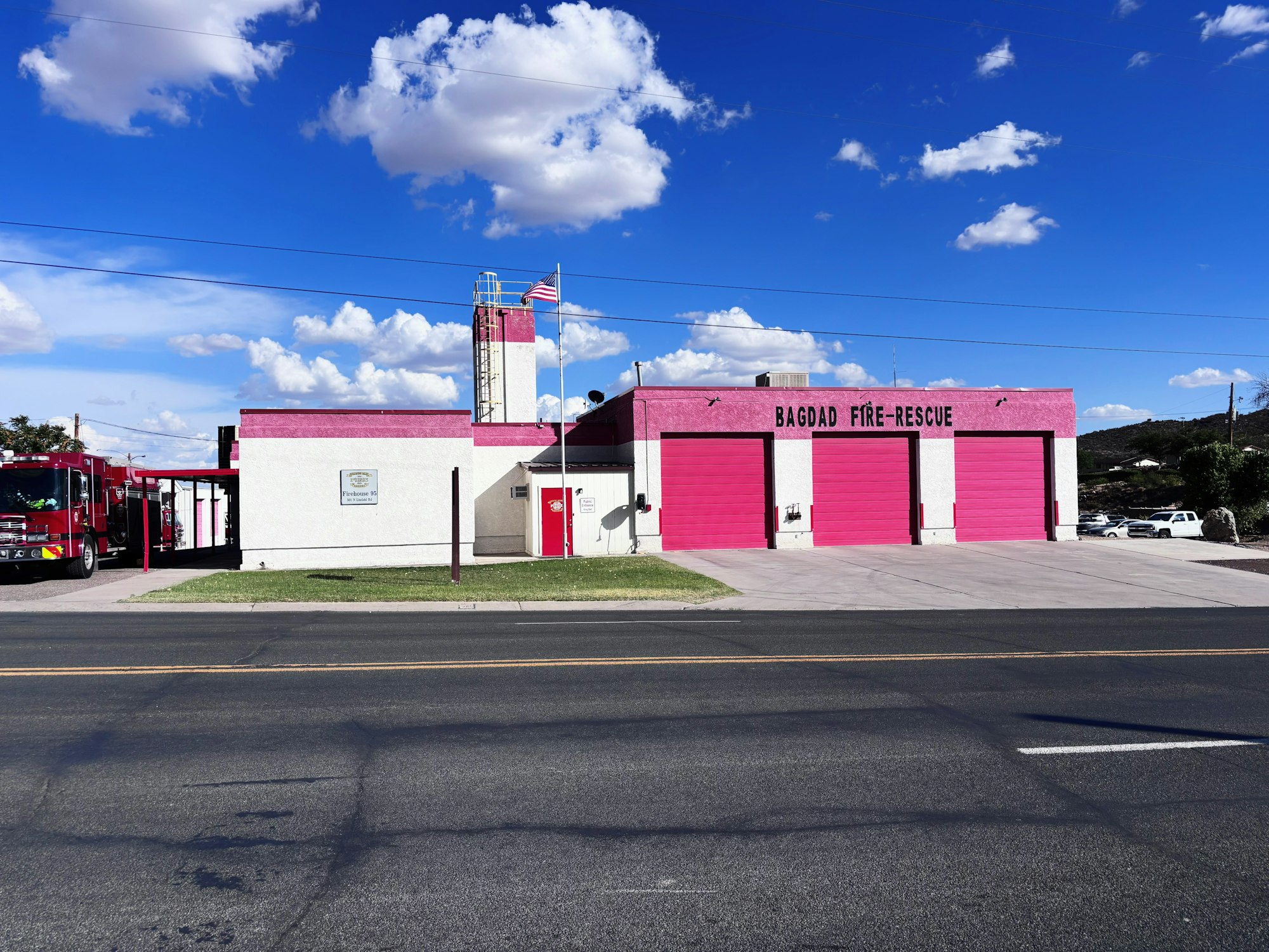 Bagdad Fire-Rescue building with pink doors, fire trucks visible, and an American flag flying.