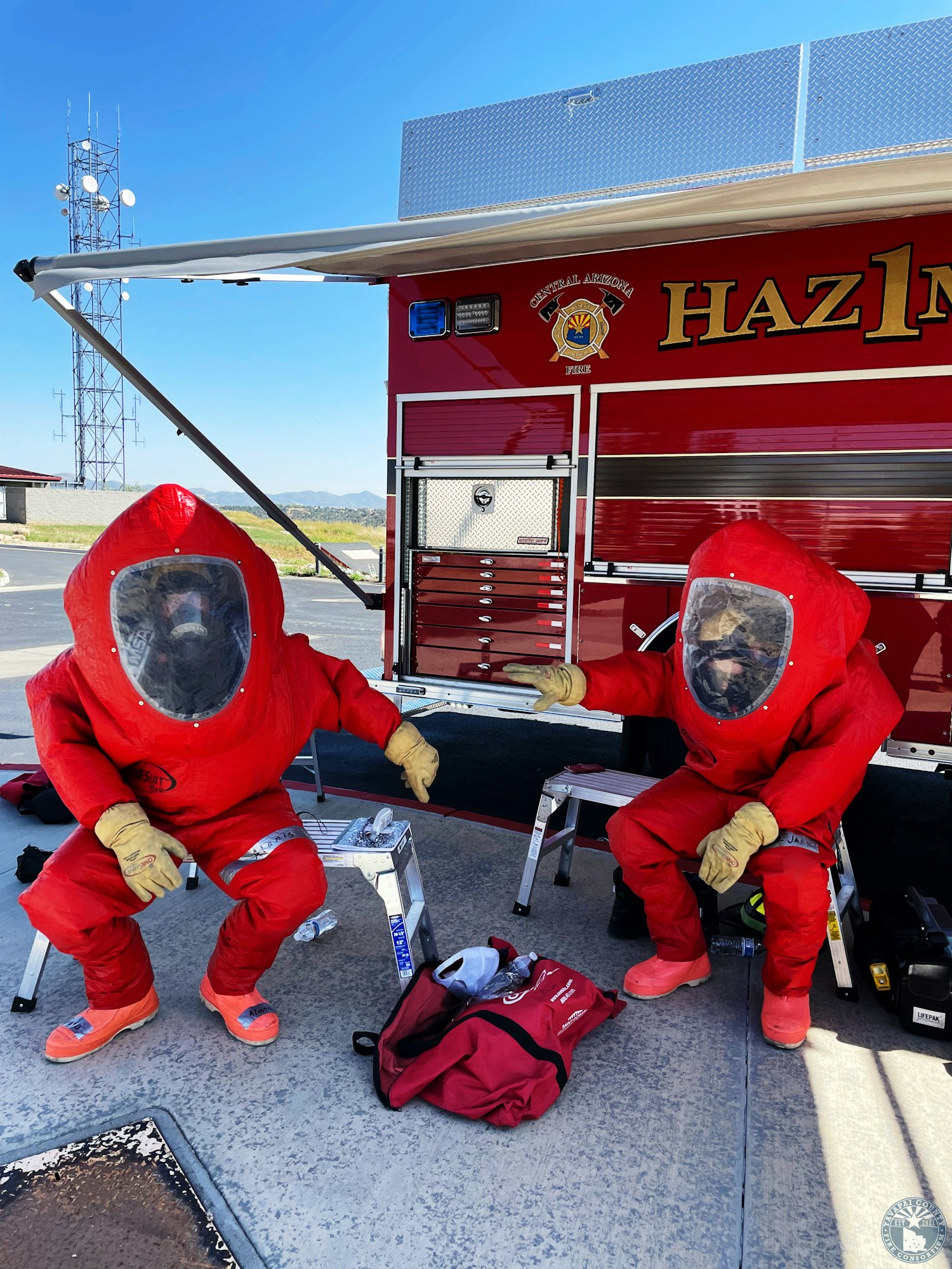 Two people in red hazmat suits sit near a fire truck labeled "HAZ1."