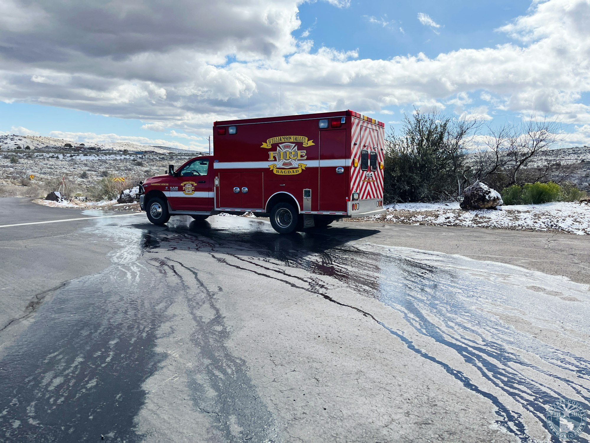 A red fire rescue vehicle parked on a wet road, snowy landscape in the background under cloudy skies.