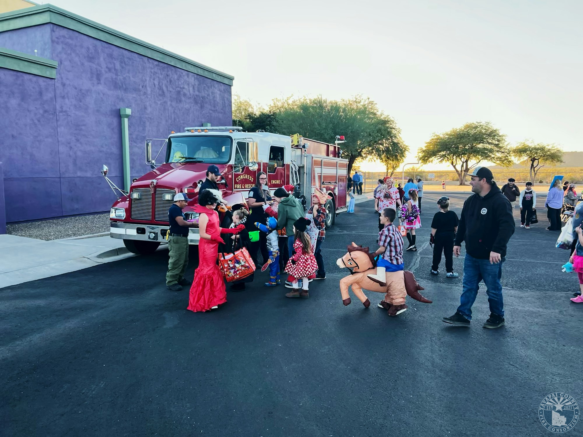 Children in costumes gather near a fire truck for a festive event.