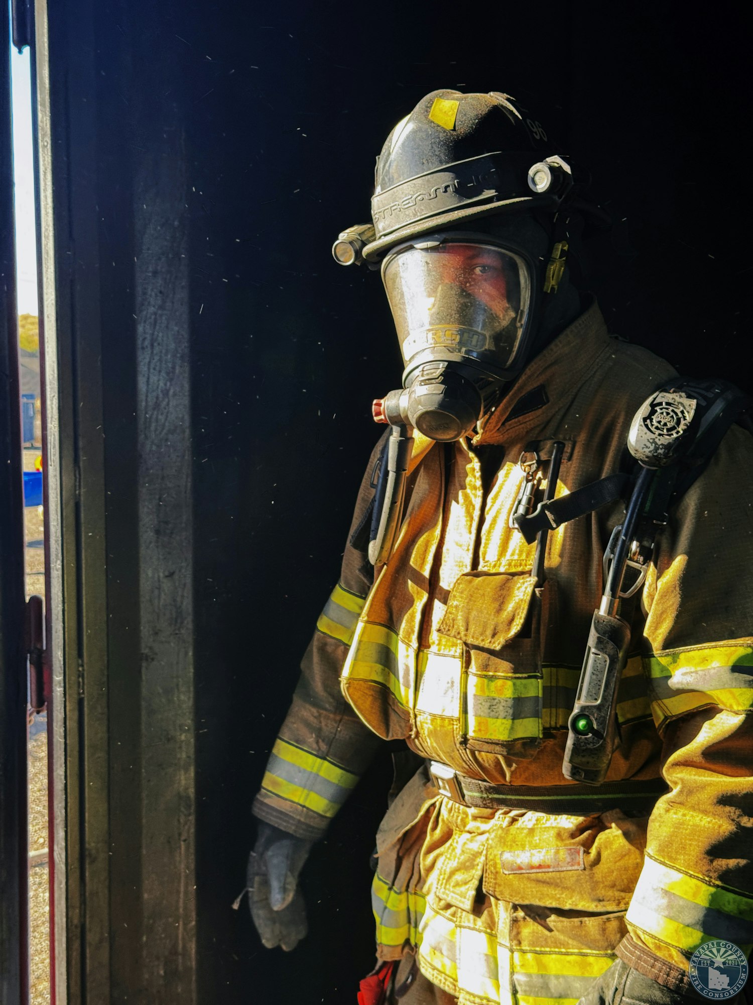 A firefighter in full gear standing in a doorway, wearing a helmet and breathing apparatus.