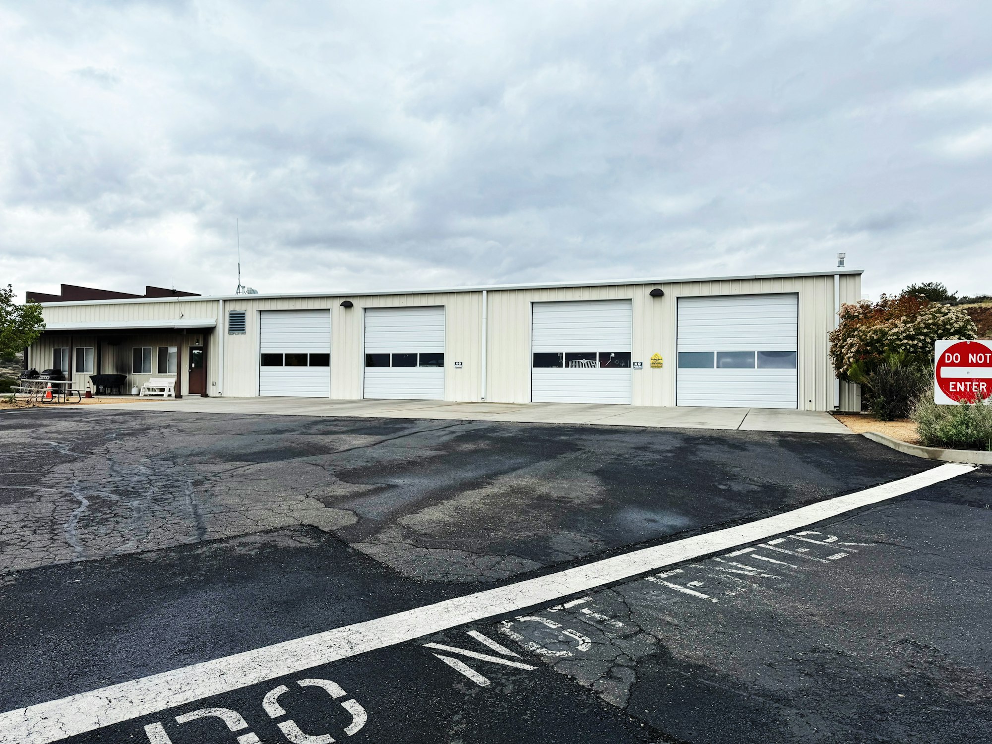 A building with three large garage doors, some foliage on the right, and a "Do Not Enter" sign in the foreground.